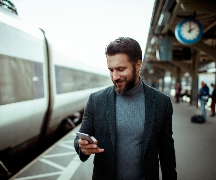 Man at train station checing his phone before boarding